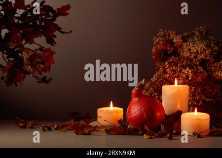 Stillleben mit Kürbis, ausgetrockneten Blättern und brennenden Kerzen. Im Hintergrund getrocknete Hortensienblüten und Eichenzweige. Herbstkonzept. Stockfoto