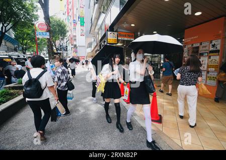 Zwei Mädchen im Teenageralter, die Regenschirme tragen, spazieren auf dem Pavememt in Shibuya, Tokio, Japan Stockfoto