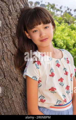 11-jähriges Mädchen, das sich an einen Baum lehnt Stockfoto