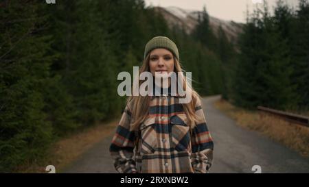 Blonde Reisende, die Kamera anschaut, während sie durch die Straße in den Bergen spaziert Stockfoto