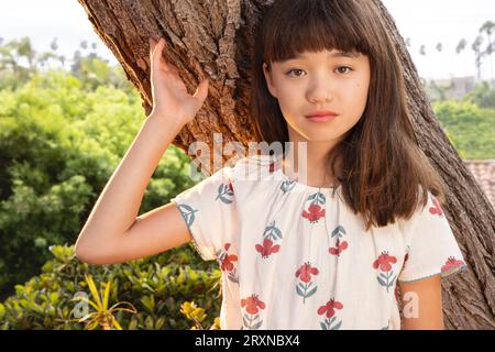 Elf Jahre altes Mädchen, das sich an einen Baum lehnt Stockfoto