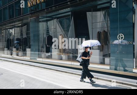 Eine Frau, die einen Schirm hält, spaziert an einem High-End-Geschäft in Ginza, Tokio, Japan vorbei Stockfoto