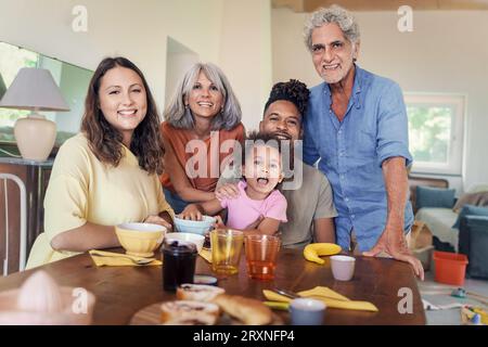 Eine fröhliche Großfamilie, einschließlich Großeltern, Eltern und einem zweirassigen Kind, posiert gemeinsam in einer geräumigen, sonnendurchfluteten Küche für ein Familienporträt. Stockfoto