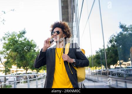 Lässiger, stylischer afroamerikanischer Mann, der mit einer Tasche zum Telefonieren geht Stockfoto