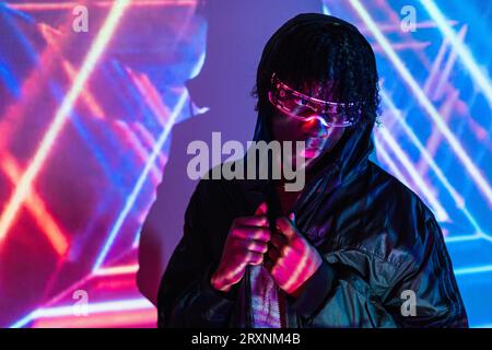 Studio-Porträt mit violetten und blauen Neonlichtern eines modernen Mannes mit futuristischer Brille Stockfoto