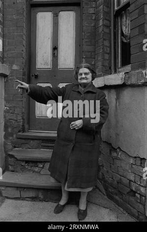 Eine ältere Dame stand vor ihrem viktorianischen Reihenhaus, das während der Räumung des Slums von St Ann's, Nottingham, England, auf den Abriss wartet. Stockfoto