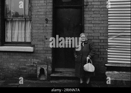 Eine ältere Dame stand vor ihrem viktorianischen Reihenhaus, das während der Räumung des Slums von St Ann's, Nottingham, England, auf den Abriss wartet. Stockfoto