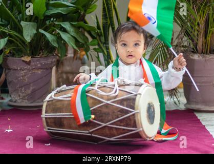 Niedliches Kleinkind mit indischer Trikolorfahne, traditionellem Dholak und Tuch mit unschuldigem Gesicht Stockfoto
