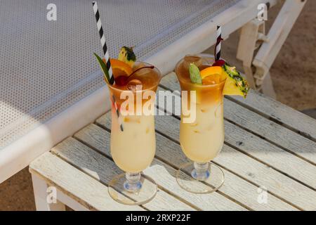 Nahansicht von zwei Gläsern Cocktail auf weißem Tisch am Sandstrand unter Sonnenliegen. Curacao. Stockfoto