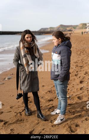 Zwei Frauen plaudern am Sandstrand mit Klippen im Hintergrund, West Bay Dorset Stockfoto