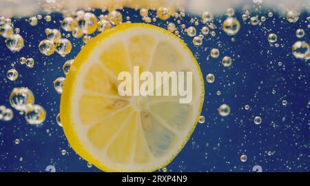 Unter Wasser mit frisch gepresster gesüßter Limonade, die rohe Zitronen in Soda-Wasser vor dunkelblauem oder schwarzem Hintergrund schneiden. Nahaufnahme Limonade Stockfoto