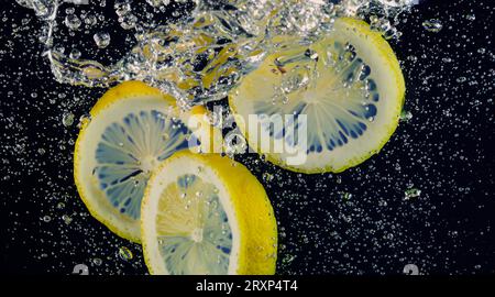 Unter Wasser mit frisch gepresster gesüßter Limonade, die rohe Zitronen in Soda-Wasser vor dunkelblauem oder schwarzem Hintergrund schneiden. Nahaufnahme Limonade Stockfoto