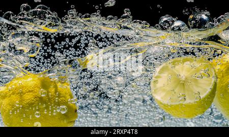 Unter Wasser mit frisch gepresster gesüßter Limonade, die rohe Zitronen in Soda-Wasser vor dunkelblauem oder schwarzem Hintergrund schneiden. Nahaufnahme Limonade Stockfoto