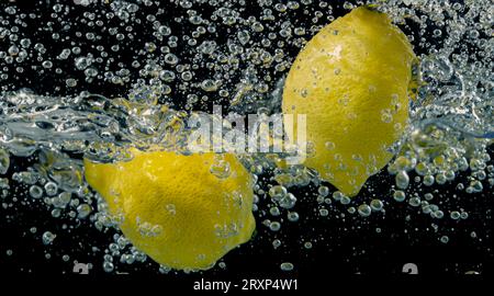 Unter Wasser mit frisch gepresster gesüßter Limonade, die rohe Zitronen in Soda-Wasser vor dunkelblauem oder schwarzem Hintergrund schneiden. Nahaufnahme Limonade Stockfoto