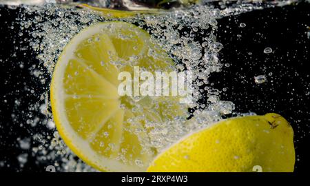 Unter Wasser mit frisch gepresster gesüßter Limonade, die rohe Zitronen in Soda-Wasser vor dunkelblauem oder schwarzem Hintergrund schneiden. Nahaufnahme Limonade Stockfoto