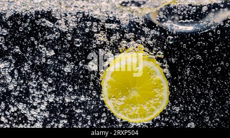 Unter Wasser mit frisch gepresster gesüßter Limonade, die rohe Zitronen in Soda-Wasser vor dunkelblauem oder schwarzem Hintergrund schneiden. Nahaufnahme Limonade Stockfoto