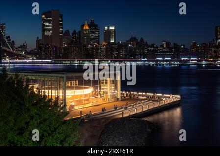 Einzigartiger Blick auf das Jane's Karussell im Brooklyn Bridge Park in Blue Hour. Manhattan's Two Bridges Area und East River im Vordergrund. Stockfoto