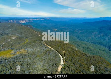 Drohnen-Luftaufnahme der Kedumba Valley Road, die sich entlang der Klippe durch den Wald von Gummibäumen in den Blue Mountains in Australien schlängelt Stockfoto