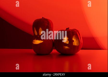 Zwei Jack-o-Laternen leuchten im Dunkeln auf rotem Hintergrund. Halloween Dekoration. Stockfoto