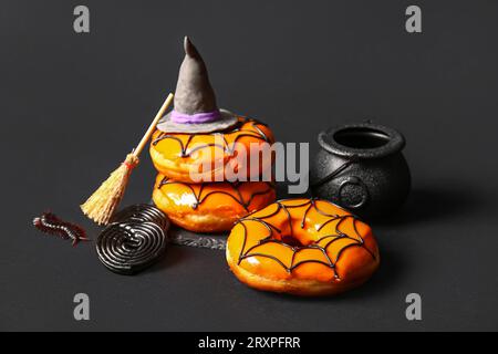 Leckere Donuts mit Dekorationen für Halloween auf schwarzem Hintergrund Stockfoto