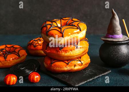 Tafel mit leckeren Donuts für Halloween mit Süßigkeiten, Topf und Hexenhut auf schwarzem Hintergrund Stockfoto