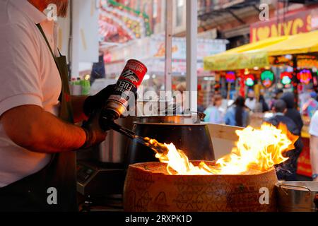 Ein Mrs Claus Cafe Koch schmilzt ein Rad Grana Padano mit einer Taschenlampe, um Cheese Wheel Pasta zu machen, beim San Gennaro Feast, New York City. Stockfoto