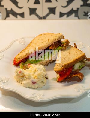 BLT, ein Sandwich mit Speck, Tomaten und Salat aus Haferbrot, mit einer Portion Kartoffelsalat auf einem weißen Teller. USA. Stockfoto