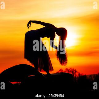 Silhouette einer langhaarigen Frau, die gegen die untergehende Sonne posiert Stockfoto