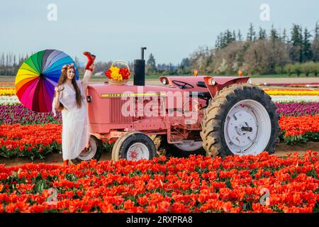 Frau, die einen bunten Regenschirm hält und sich auf dem rostigen Traktor teilt Stockfoto