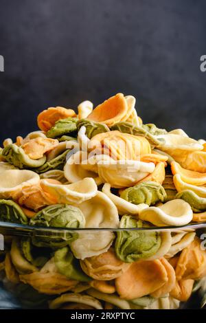Getrocknete dreifarbige Orecchiette-Pasta in einer Glasschale im Profil: Eine Schüssel ungekochter Orecchiette-Pasta in einer Glasschale von der Seite gesehen Stockfoto