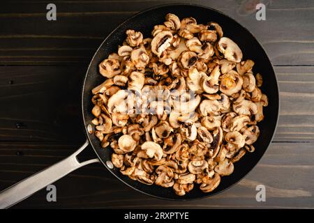 In Scheiben geschnittene Knopfpilze in einer großen antihaftbeschichteten Bratpfanne: Scheiben weißer Pilze, die geschmolzene Butter in einer großen antihaftbeschichteten Pfanne kochen Stockfoto