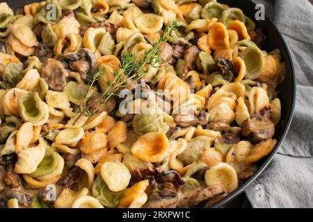 Orecchiette mit Pilz-Thymian-Sauce in einer Pfanne: Nudeln und Pilze in Sahnesauce, serviert in einer großen Bratpfanne Stockfoto