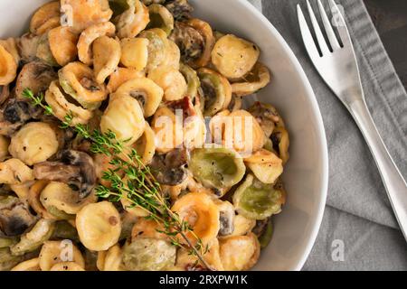 Orecchiette mit Pilz-Thymian-Sauce in einer Pasta-Schüssel: Nudeln und Pilze in Sahnesauce, serviert in einer großen flachen Schüssel Stockfoto