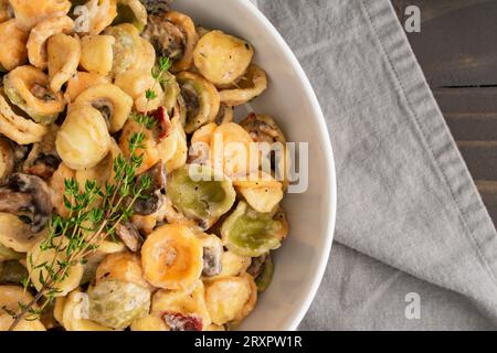 Orecchiette mit Pilz-Thymian-Sauce in einer Pasta-Schüssel: Nudeln und Pilze in Sahnesauce, serviert in einer großen flachen Schüssel Stockfoto