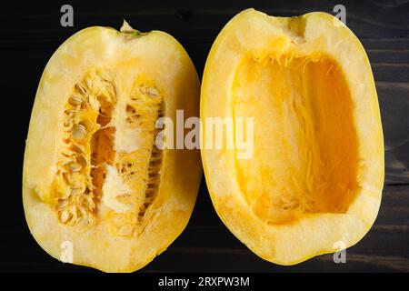 Spaghetti-Kürbis in Scheiben mit einer Seite gesät: Halbierter Spaghetti-Kürbis mit und ohne Samen aus nächster Nähe auf einem Holztisch Stockfoto
