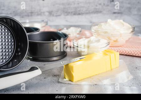 Käsekuchen-Rezept. Drei kleine runde Kuchenpfannen (Dose, Schimmel), Butter und einige Zutaten für das Käsekuchen-Rezept aus nächster Nähe auf dem Küchentisch Stockfoto