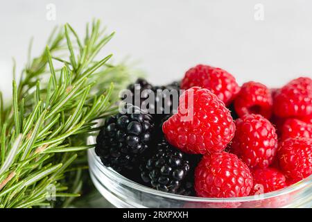 Himbeeren und Brombeeren und Rosmarin aus nächster Nähe. Frische Beeren in einer Schüssel aus nächster Nähe Stockfoto