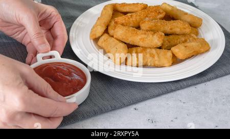 Fischstäbchen in einer knusprigen goldenen Panade und eine Schüssel Ketchup aus nächster Nähe auf dem Küchentisch Stockfoto