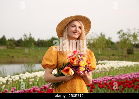 Glückliche Frau mit Frühlingsstrauß von Blumen in schönem Tulpenfeld an sonnigen Tagen Stockfoto