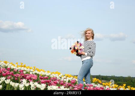 Glückliche Frau mit Frühlingsstrauß von Blumen in schönem Tulpenfeld an sonnigen Tagen Stockfoto