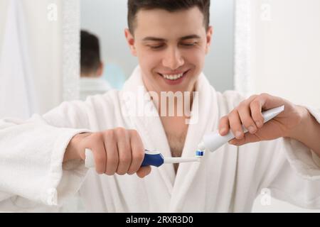 Mann, der Zahnpasta aus der Tube auf die elektrische Zahnbürste im Badezimmer drückt, selektiver Fokus Stockfoto