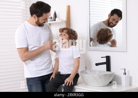 Vater hilft seinem Sohn, im Bad Zähne zu putzen Stockfoto