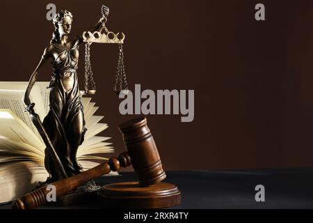Statue von Lady Justice in der Nähe von Gavel und offenem Buch auf dunklem Tisch, Platz für Text. Symbol der gerechten Behandlung nach dem Gesetz Stockfoto