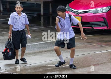 SAMUT PRAKAN, THAILAND, SEP 20 2023, fröhliche Schuljungen in Uniform spielen Spiele auf der regnerischen Straße Stockfoto