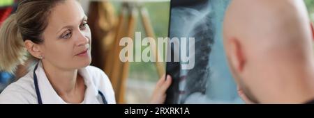 Ärztin hält Röntgenbild und Stift in den Händen und spricht mit männlichem Patienten. Stockfoto