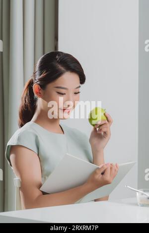 Asiatische Frau liest ein Buch und hält grünen Apfel im Haus Stockfoto