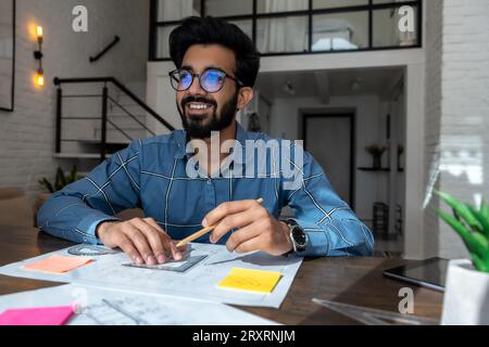 Dunkelhaariger junger Mann, der am Tisch sitzt und einen Projektentwurf vorbereitet Stockfoto