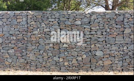 Stein texturierter Zaun Gabion Stahl Metall Gitter Stein Wandkorb aus Mesh und Stein Hintergrund Wand horizontale Fassade Stockfoto