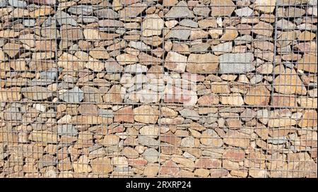 Hintergrund Gabionenzaun Stahl Metall Gitterstein Wand großer Käfig Korb Wand Restauration Fassadenwand Steine Tapete Stockfoto