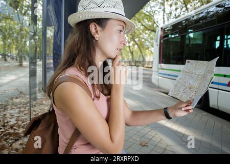 Frau, die eine Karte liest, während sie an der Bushaltestelle wartet Stockfoto